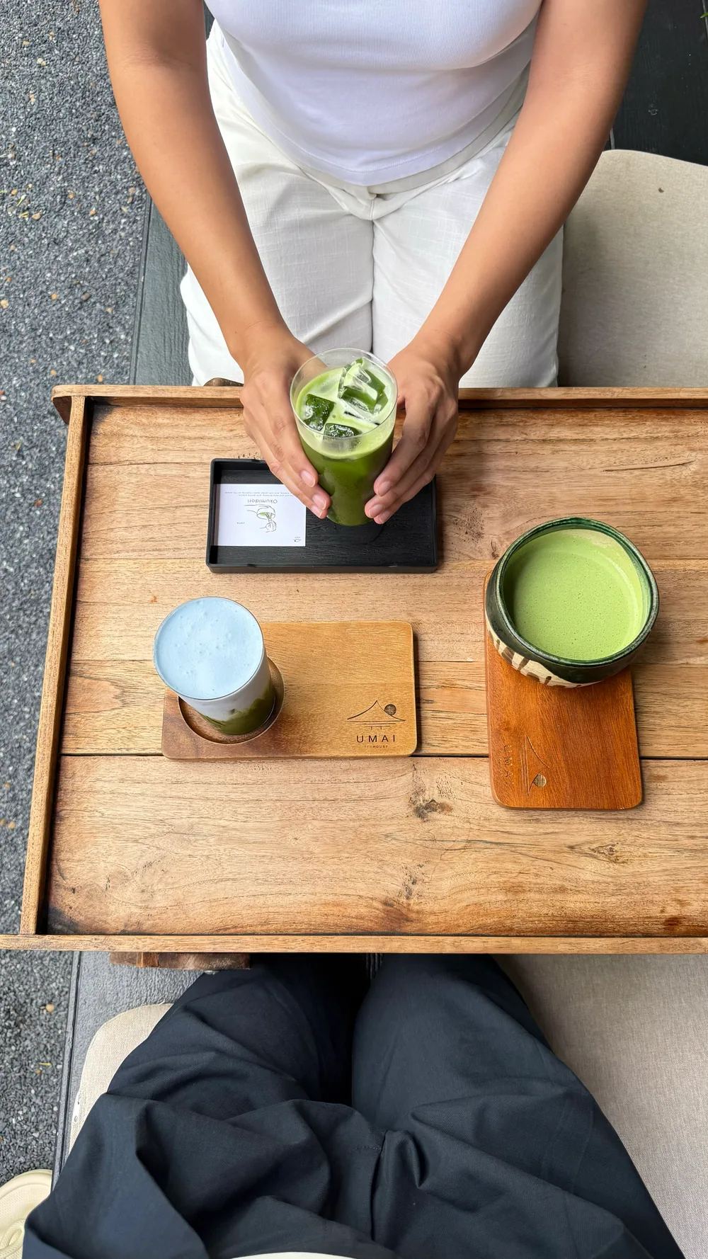 Hands holding a green iced drink above a wooden table with two more drinks