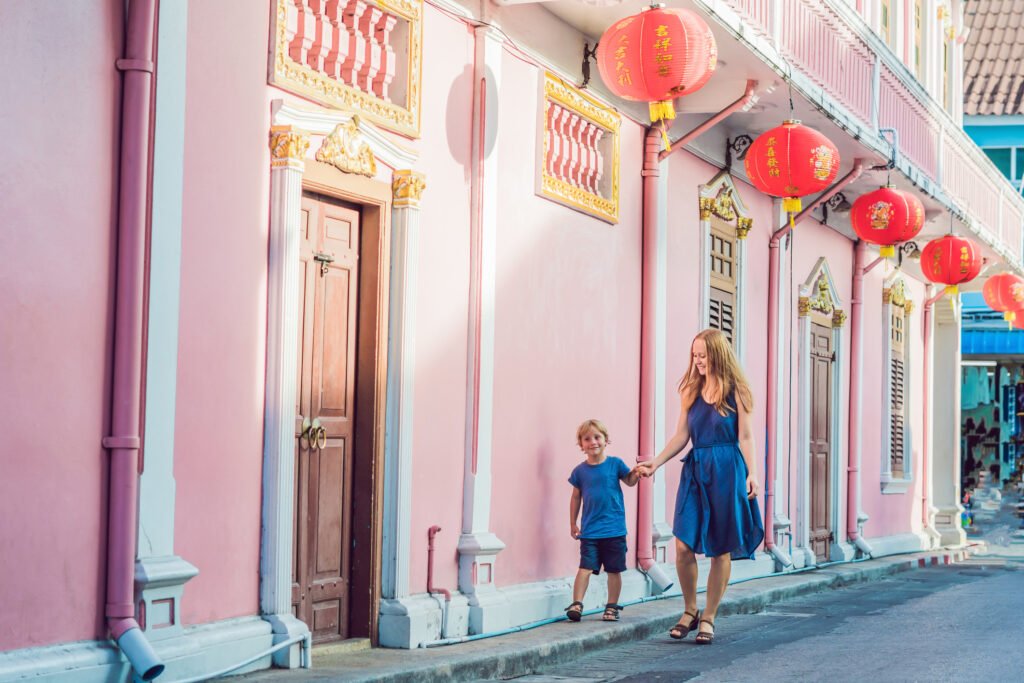 A woman and child walking past pink shophouses and red lanterns