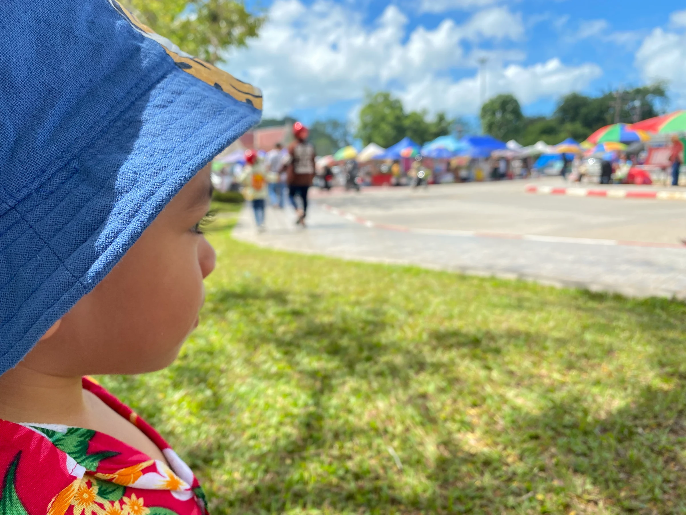 A child wearing a blue sun hat and floral shirt looking across a sunny outdoor space