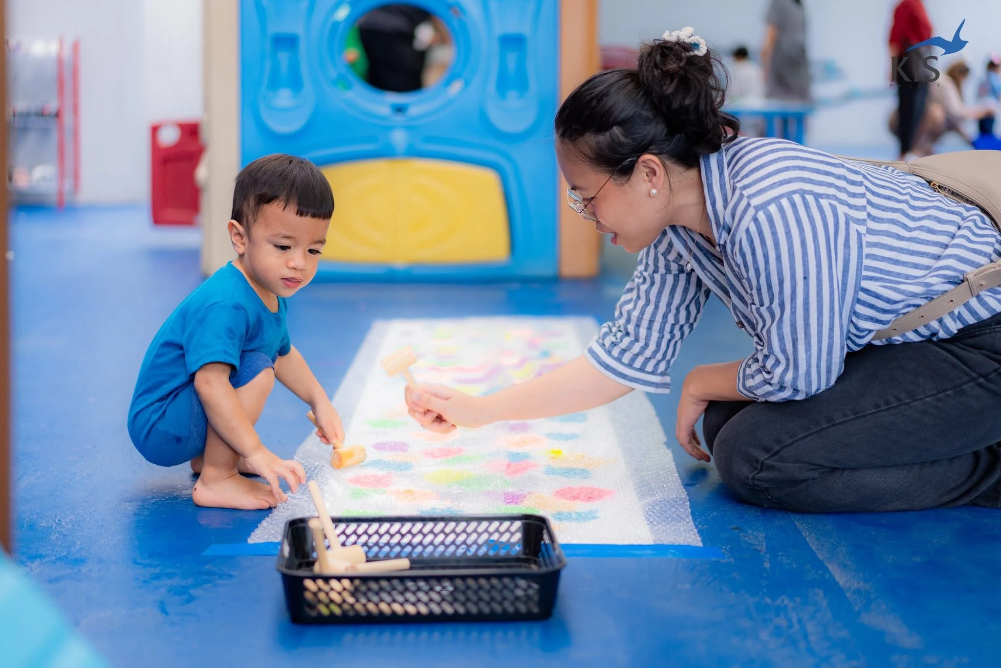 A woman and child painting together on the floor of a colorful activity room