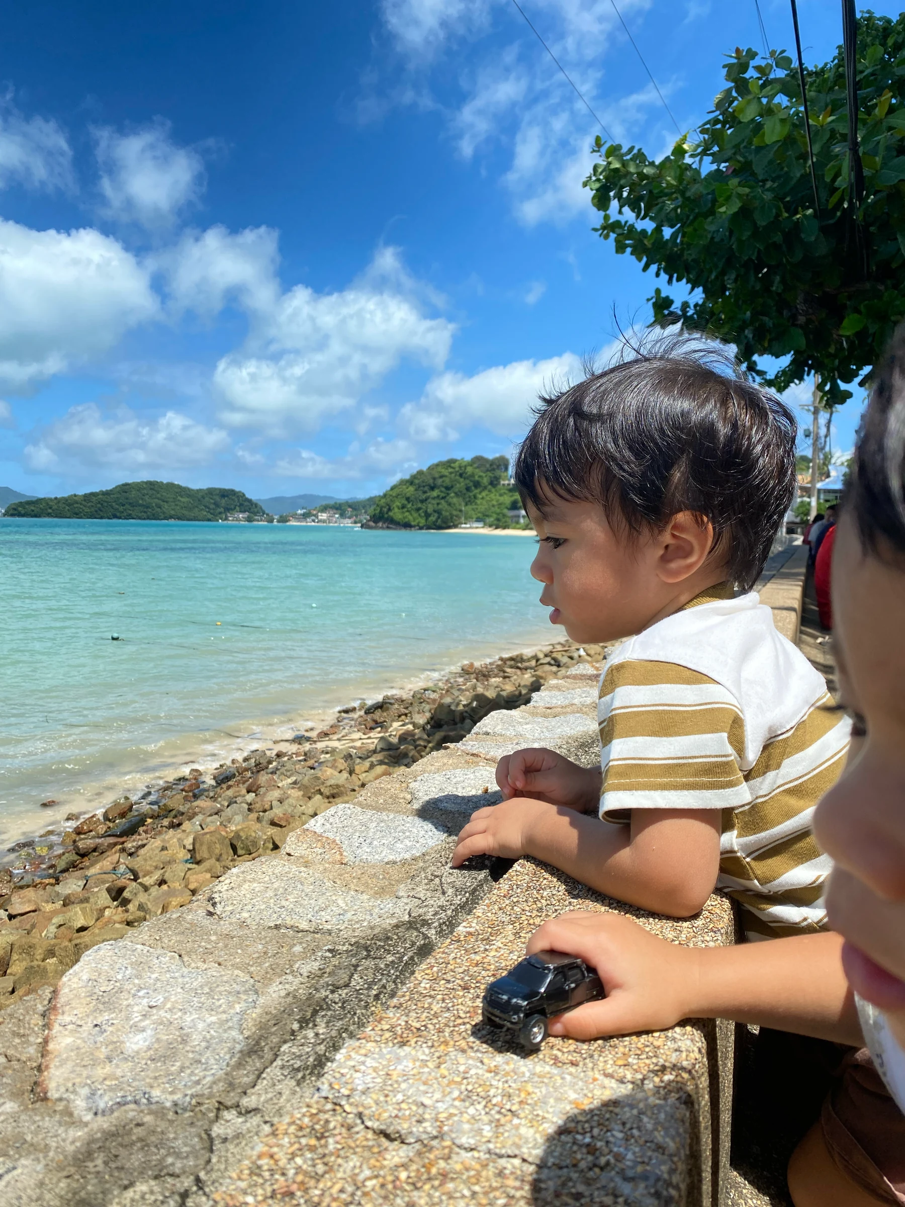 A child sitting on rocks beside turquoise sea water on a sunny day
