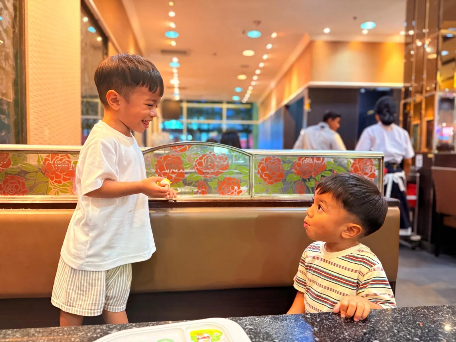 Two children sharing a playful moment beside a restaurant booth